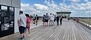 Menschen lesen sich auf der Dachterrasse des THF Towers Schilder durch. Im Hintergrund blauer Himmel