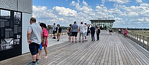 Menschen lesen sich auf der Dachterrasse des THF Towers Schilder durch. Im Hintergrund blauer Himmel
