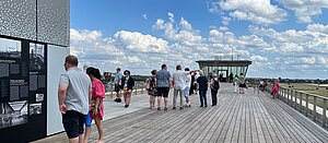 Menschen lesen sich auf der Dachterrasse des THF Towers Schilder durch. Im Hintergrund blauer Himmel