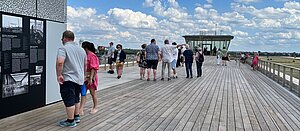 Menschen lesen sich auf der Dachterrasse des THF Towers Schilder durch. Im Hintergrund blauer Himmel