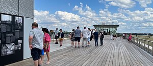 Menschen lesen sich auf der Dachterrasse des THF Towers Schilder durch. Im Hintergrund blauer Himmel