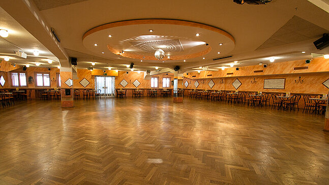 Festlicher Ballsaal der Tanzschule Traumtänzer am Flughafen Tempelhof, am Rand der Tanzfläche stehen Stühle und Tische.