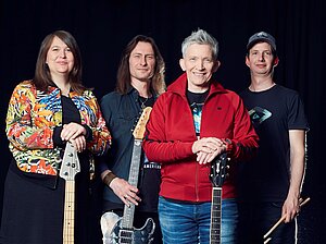 Die Musikerin Suli Puschband mit posiert gemeinsam mit drei anderen Musiker:innen vor schwarzem Hintergrund.