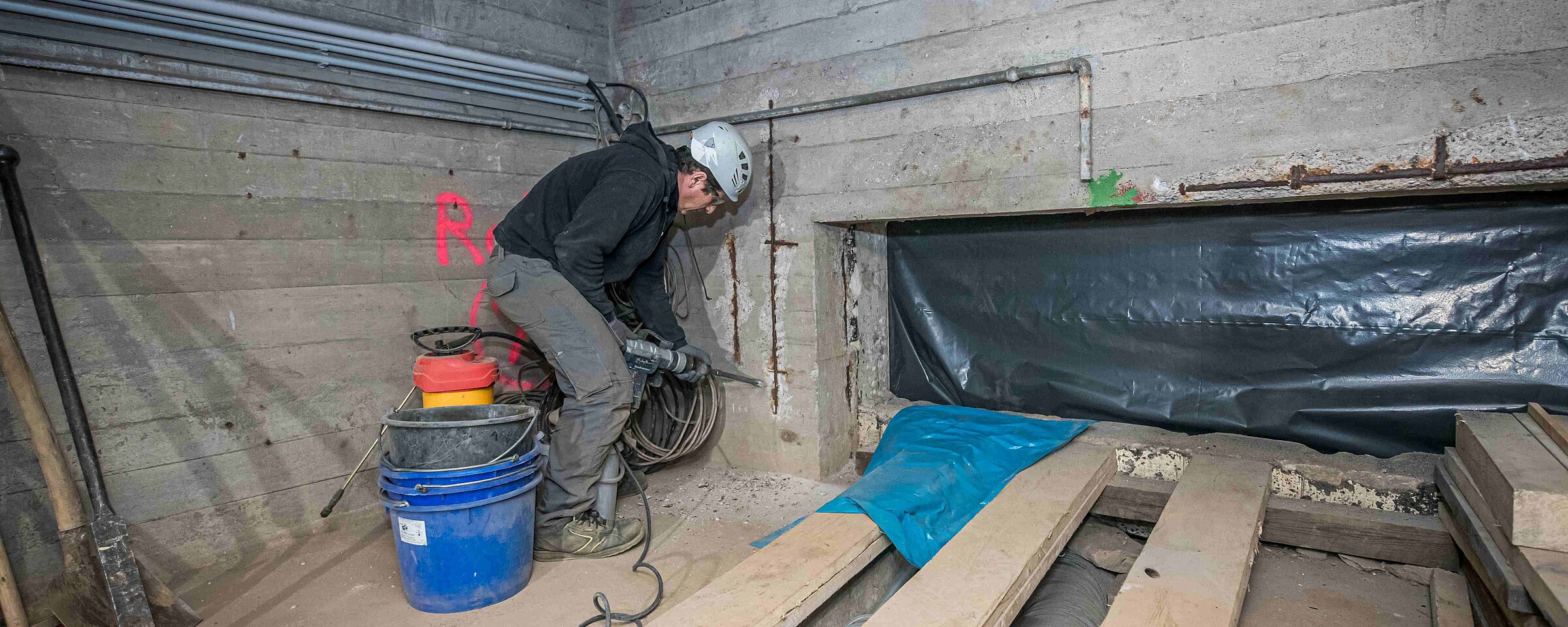 Bauarbeiter unter Tage, der an einer Mauer bohrt