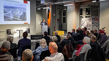 Publikum schaut auf Render am Rednerpult vor einer Leinwand mit dem Flughafen Tempelhof