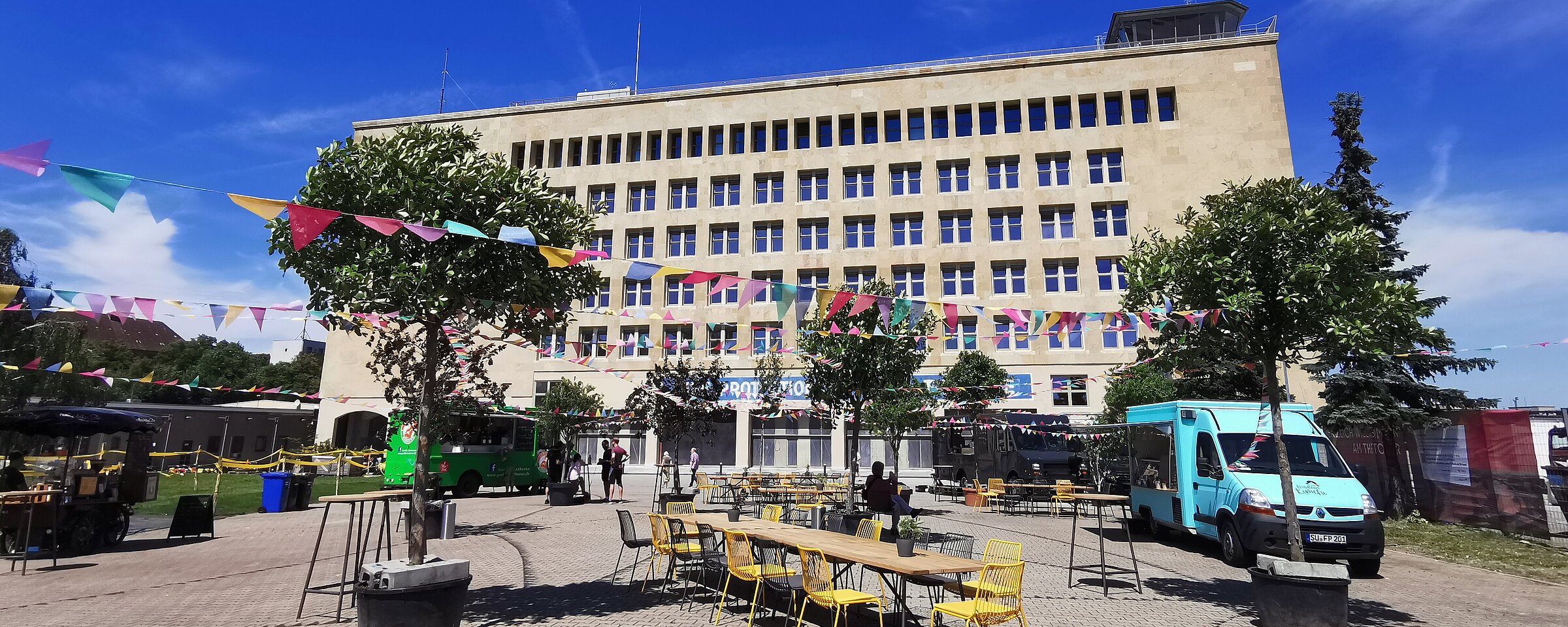Blick auf die Außenfassade des THF TOWER. Auf der Außenfläche stehen Foodtrucks 