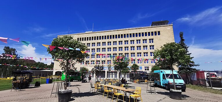 Blick auf die Außenfassade des THF TOWER. Auf der Außenfläche stehen Foodtrucks 