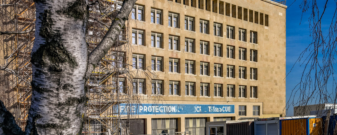 Hinter dem Stamm einer Birke ist der Kopfbau West mit Baugerüst und Baustelle