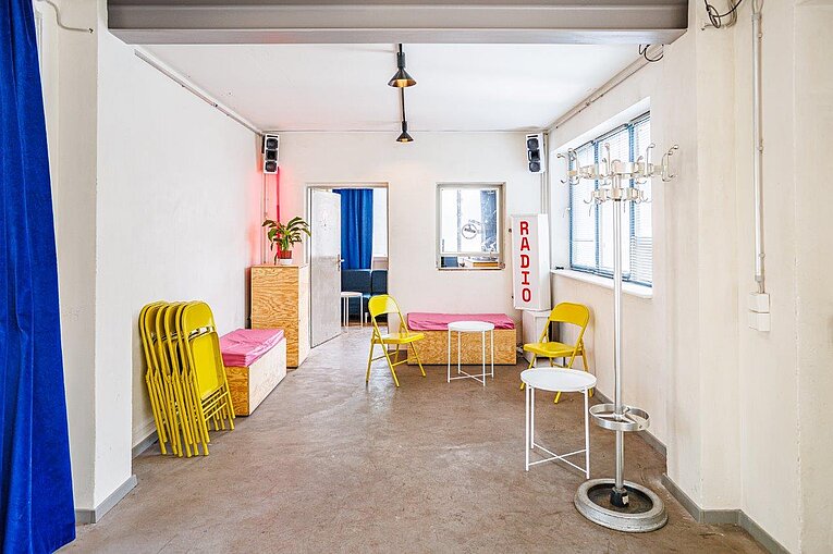 Kreativ gestalteter Raum im Torhaus des Flughafen Tempelhof mit farbigen Vorhängen, Sitzmöbeln und Tageslicht aus historischen Fenstern