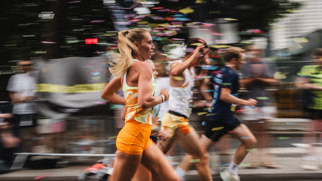 Läufer eines Marathons laufen auf einer Straße durch Konfetti. Im Hintergrund sieht man verschwommen Zuschauer:innen 