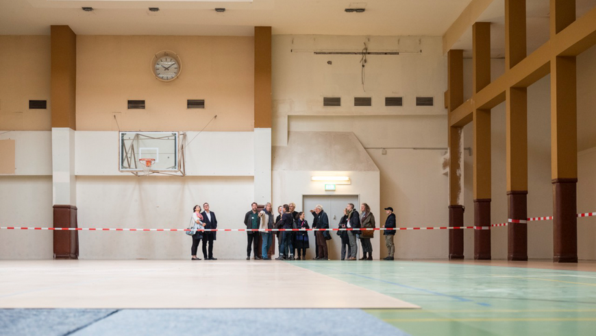 Eine Gruppe von Menschen steht in der ehemaligen Basketballhalle im Flughafen Tempelhof