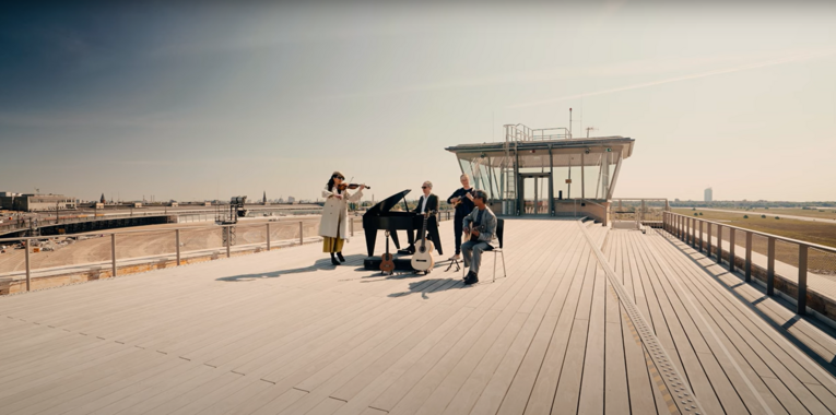 Ein Quartett mit einem Flügel steht auf dem Dach des THF TOWERs und musiziert gemeinsam. Im Hintergrund das Tempelhofer Feld und der Fluglotsen Tower
