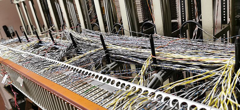 in dichtes Geflecht aus hunderten bunten Netzwerkkabeln (Patchkabeln) in Blau, Gelb und Weiß hängt ungeordnet vor den Racks in der Telefonzentrale des Flughafen Tempelhof