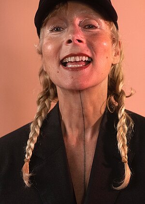 Porträt von DJ Femalemachovon rotem Hintergrund. Sie trägt ein schwarzes Jackett und zwei Zwöpfe