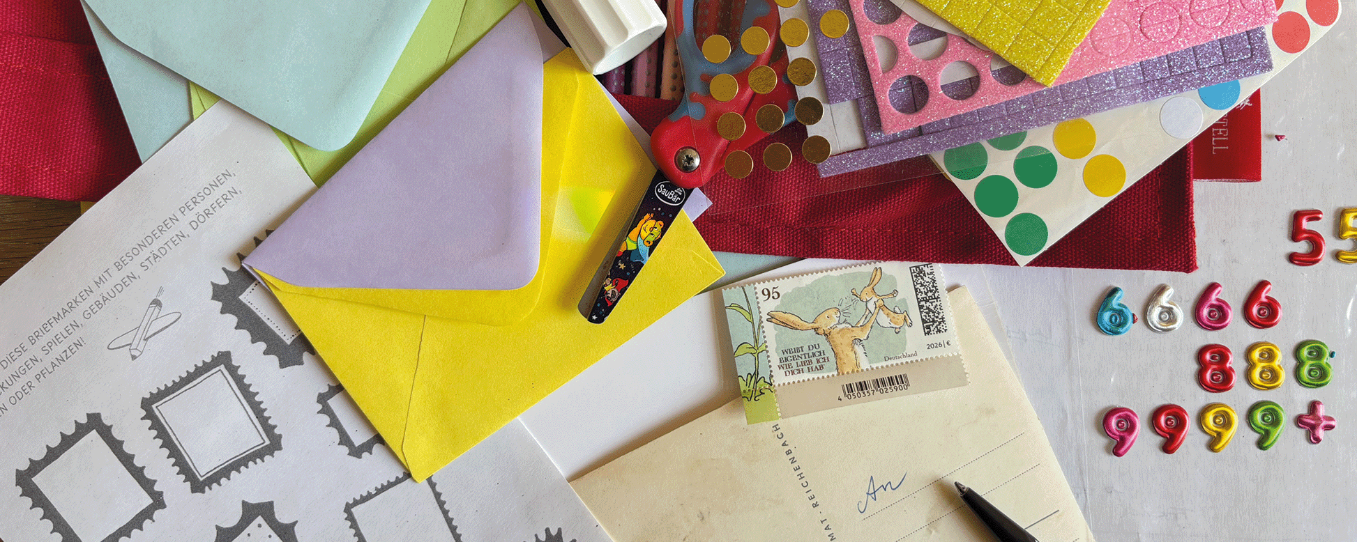 Bunte Bastelmaterialien liegen auf einer Fläche verteilt: farbige Briefumschläge, Stickerbögen mit Punkten und Glitzerstrukturen, eine Kinderschere mit Motiv, ein Klebestift, ein Stift, mehrere Briefmarken sowie ein Blatt mit vorgedruckten Briefmarkenrahmen und deutschem Text.