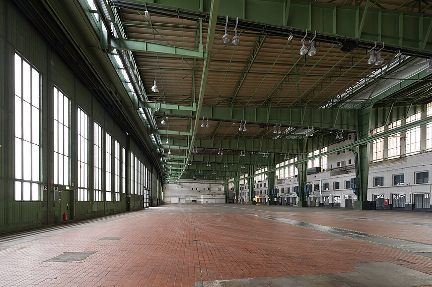 Riesige, leere Hangarhalle am Flughafen Tempelhof mit roten Ziegelsteinen am Boden und grünen Trägern