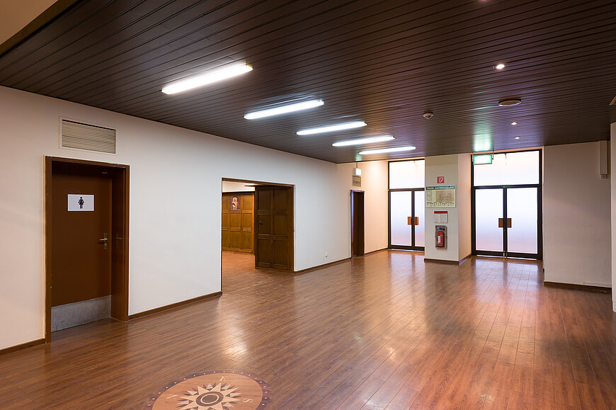 Vorraum des Flughafen Tempelhof mit Holzfußboden auf dem ein Kompass gezeichnet ist. Am Ende des Raums sind zwei Glastüren, links eine Damen-Toilette