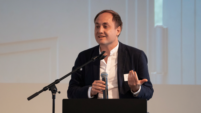 Prof. Dr. Andreas Putz mit Anzug vor einem Pult auf der Bühne der THFx Denkmalwerkstatt