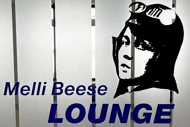 Foto von der Tür der Melli Beese Lounge am Flughafen Tempelhof mit dem Bild ihres Kopf mit einem Flughelm auf