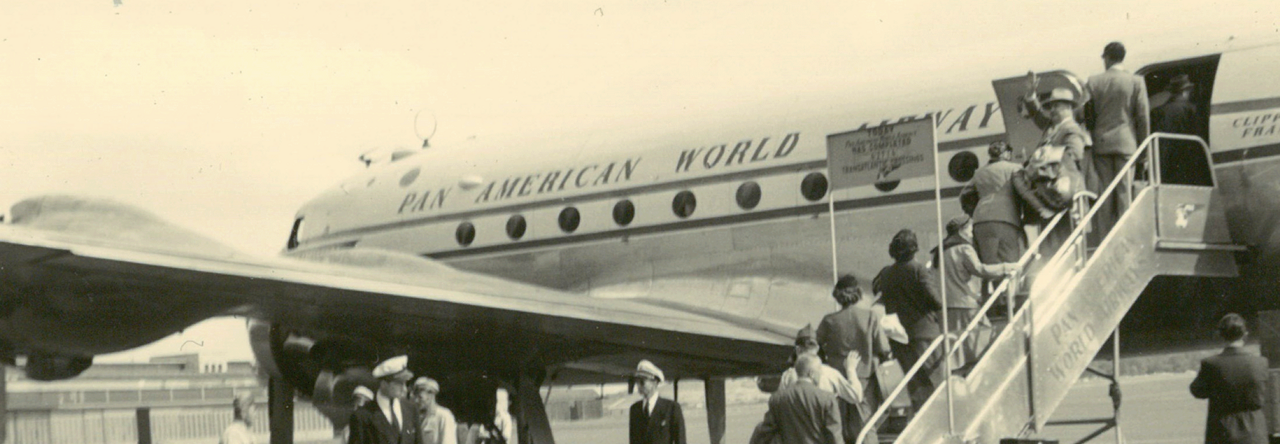 Schwarz-Weiß Foto von einem historischen Flugzeug, in das Leute über eine Treppe einsteigen