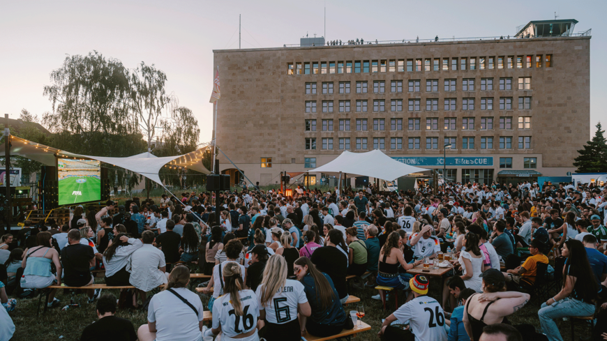 Viele Menschen sitzen beim Public Viewing im Neulich Biergarten vor dem THF TOWER