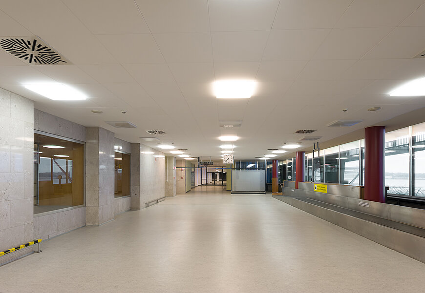 Leerer Transitgang am Flughafen Tempelhof. rechts eine gepäckablage und Fenster, durch die man auf das Vorfeld blickt. Links Fenster durch die man in die Haupthalle schaut.
