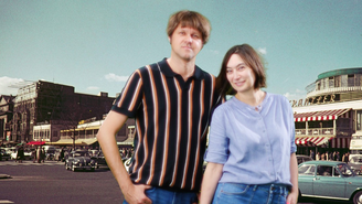 Die Band Grateful Cat steht vor einer Kulisse mit einer historischen Stadtstraße, alten Autos und Gebäuden mit Schildern und Markisen; sie tragen moderne Freizeitkleidung und bilden einen Kontrast zwischen Vergangenheit und Gegenwart.