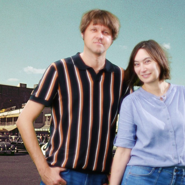 Die Band Grateful Cat steht vor einer Kulisse mit einer historischen Stadtstraße, alten Autos und Gebäuden mit Schildern und Markisen; sie tragen moderne Freizeitkleidung und bilden einen Kontrast zwischen Vergangenheit und Gegenwart.