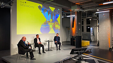 Menschen vor einer gelben Leinwand auf einer Bühne