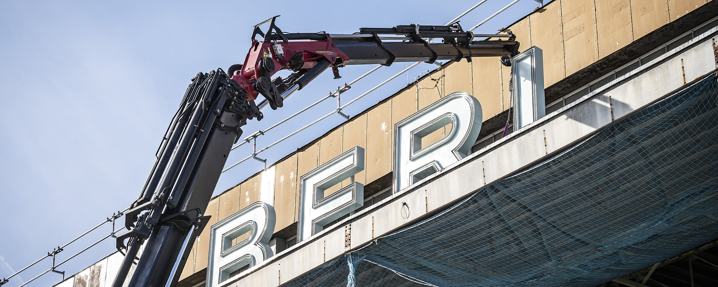 Ein Kran hebt die restaurierten Buchstaben des Schriftzugs „BERLIN – TEMPELHOF“ auf das Dach des ehemaligen Flughafens Tempelhof, um sie wieder zu montieren.