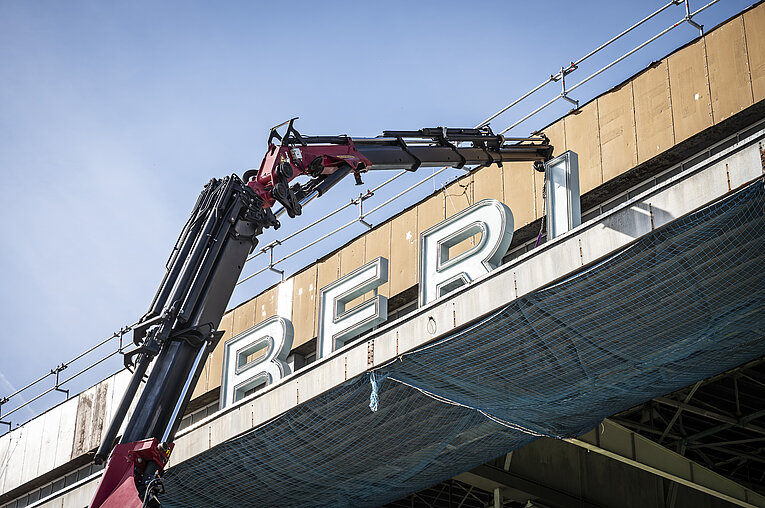 Ein Kran hebt die restaurierten Buchstaben des Schriftzugs „BERLIN – TEMPELHOF“ auf das Dach des ehemaligen Flughafens Tempelhof, um sie wieder zu montieren.