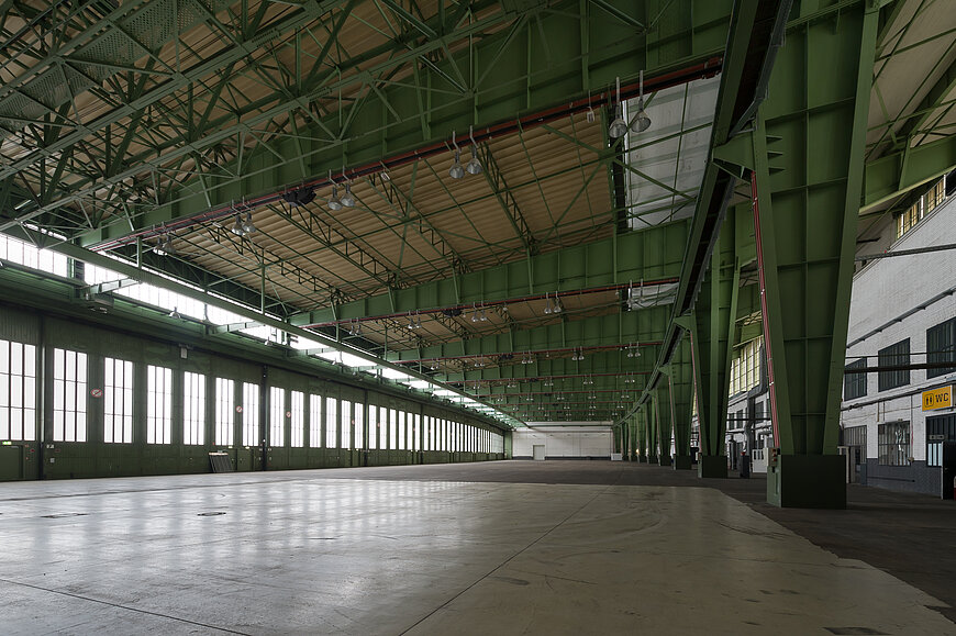 Große, leere Hangarhalle am Flughafen Tempelhof. Durch die großen fenster an der linken Front fällt Licht in die Halle