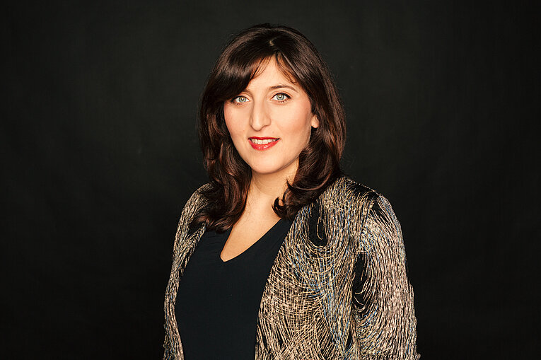 Porträt von Shanli Anwar, die vor einem schwarzen Hintergrund steht