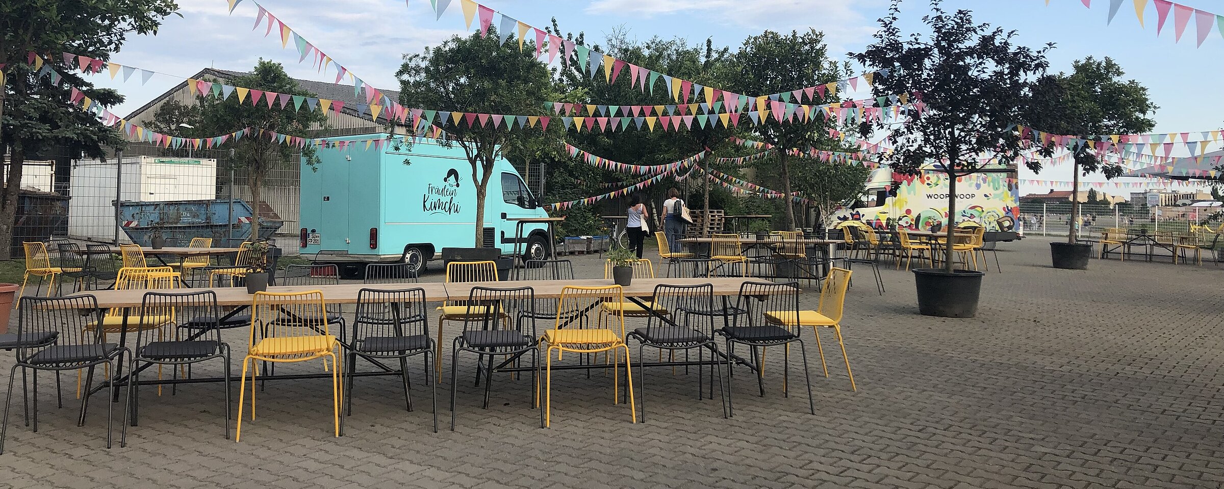 außenbereich vor dem THF TOWER mit Biergarten Tische und Stühle und einem hellblauen Sprinter 