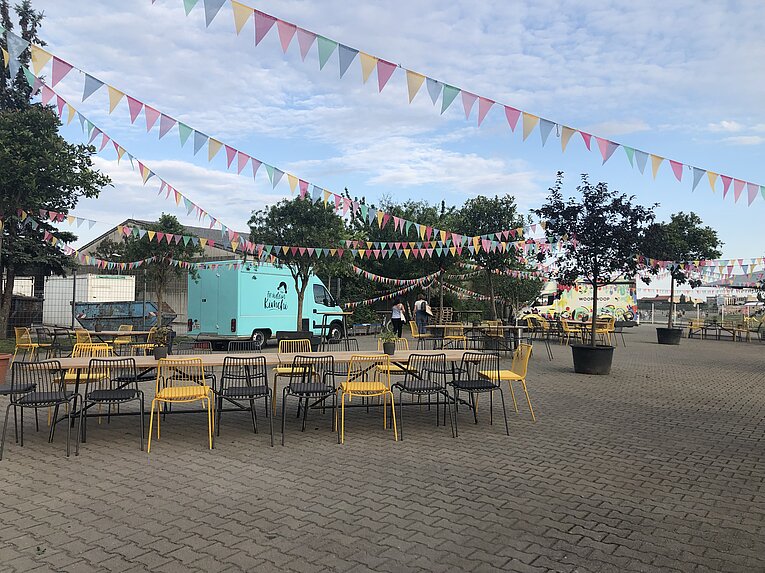 außenbereich vor dem THF TOWER mit Biergarten Tische und Stühle und einem hellblauen Sprinter 