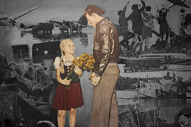 Foto von dem Gemälde in der Haupthalle des Flughafen Tempelhof, auf dem ein Soldat zu einem Mädchen runterschaut, das einen Blumenstrauß in der Hand hält und barfuß ist