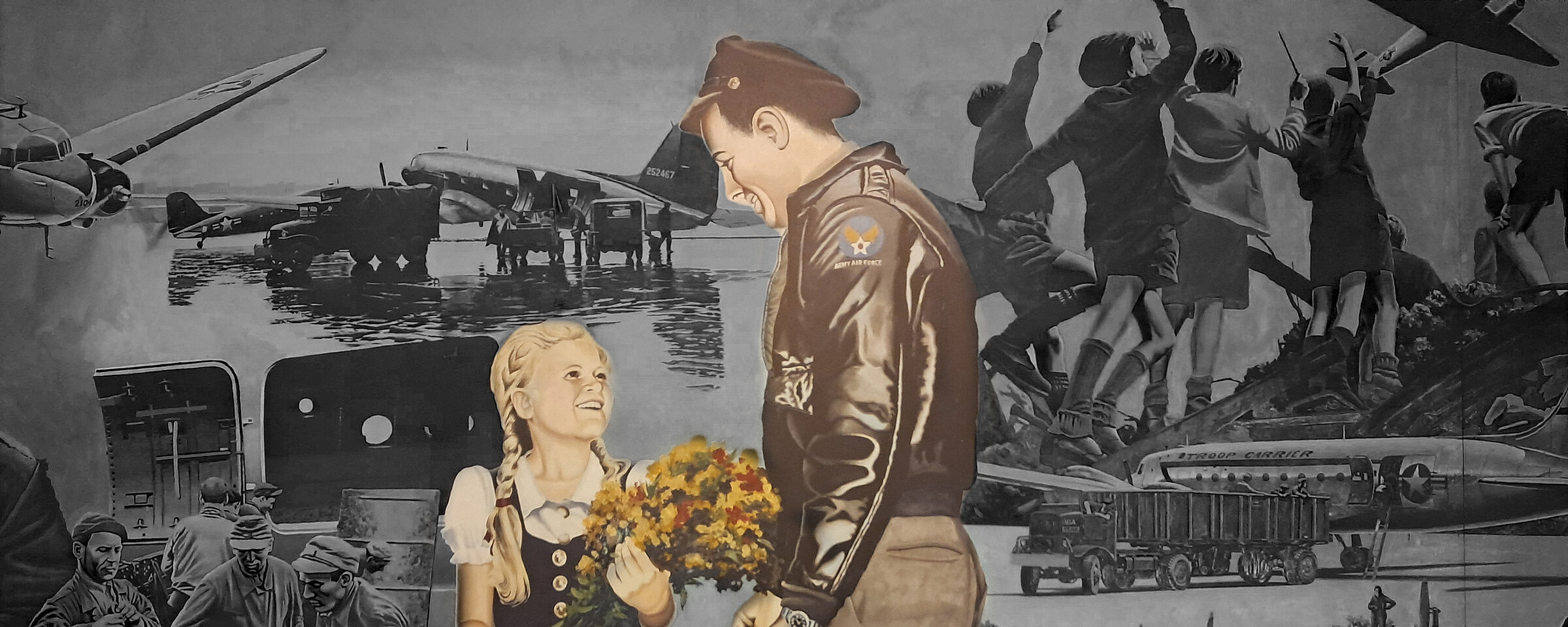 Foto von dem Gemälde in der Haupthalle des Flughafen Tempelhof, auf dem ein Soldat zu einem Mädchen runterschaut, das einen Blumenstrauß in der Hand hält und barfuß ist