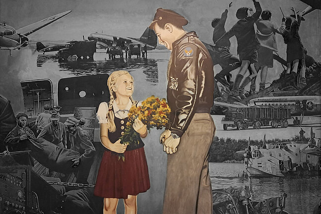 Foto von dem Gemälde in der Haupthalle des Flughafen Tempelhof, auf dem ein Soldat zu einem Mädchen runterschaut, das einen Blumenstrauß in der Hand hält und barfuß ist