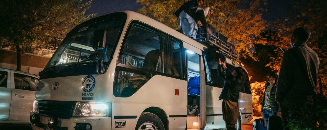 Menschen, die bei Nacht einen Kleinbus beladen und Koffer auf den Dachgepäckträger laden