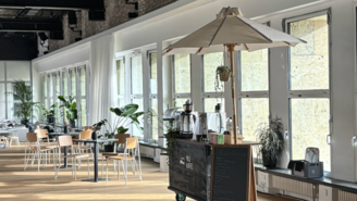 Mobile Kaffeebar mit einem Schrim im THF TOWER. Im Hintergrund Tische und Stühle sowie grüne Pflanzen. Durch die großen Fenster fällt Licht in das Café