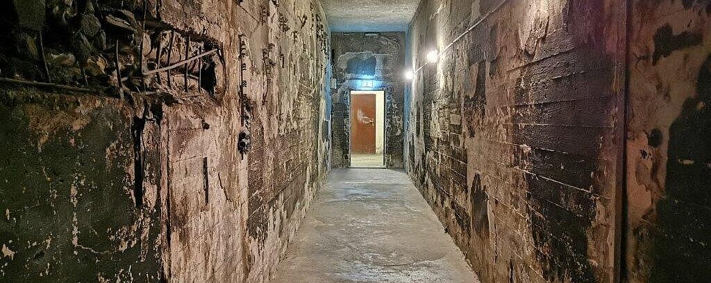 Blick in einen ausgebrannten Gang des Filmbunkers am Ende ist eine Tür über der eine Notausgangsschild angebracht ist