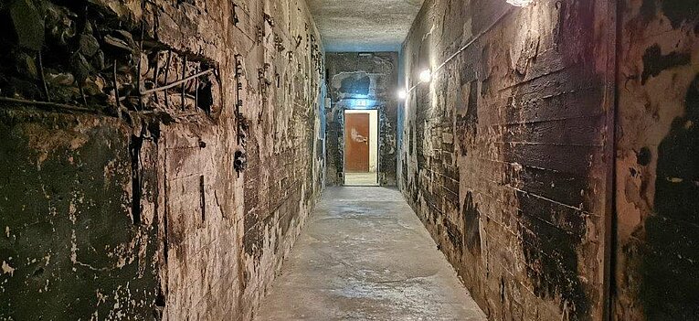 Blick in einen ausgebrannten Gang des Filmbunkers am Ende ist eine Tür über der eine Notausgangsschild angebracht ist