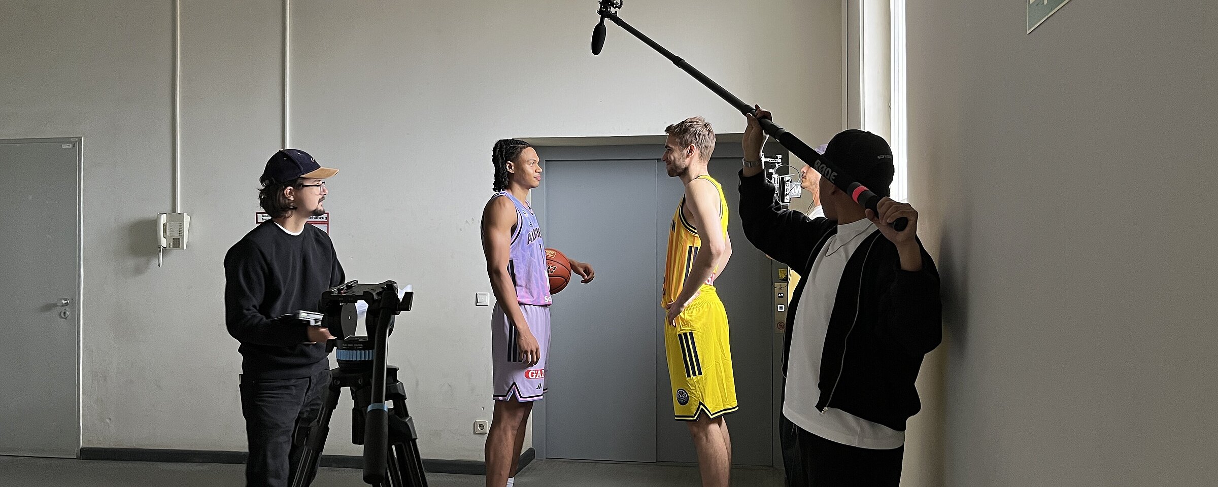 Werbefilmdreh vor einem Fahrstuhl im Flughafen Tempelhof. 2 Basketballspieler stehen vor der verschlossenen Fahrstuhltür ein Kameramann und ein Tonmann stehen vor ihnen