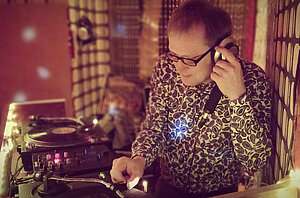 DJ Daddy Rolling Stone steht in einem kleinen, rotausgeleuchteten Raum am Mischpult. Ein Hand am Regler, die andere Hand am Kopfhörer