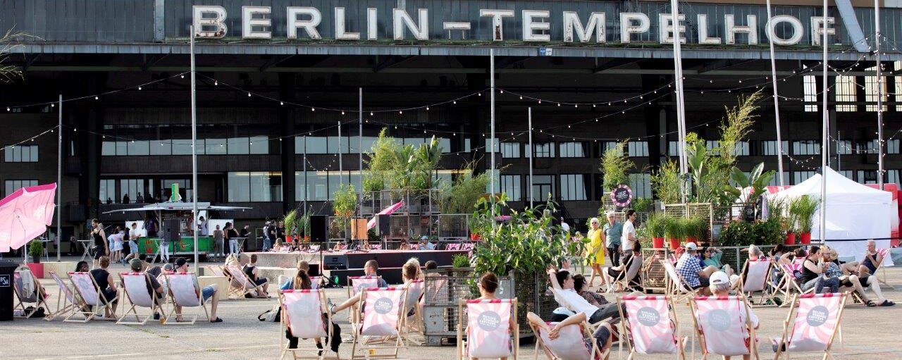 Menschen sitzen auf rosa-weiß-gestreiften Liegestühlen auf dem Vorfeld
