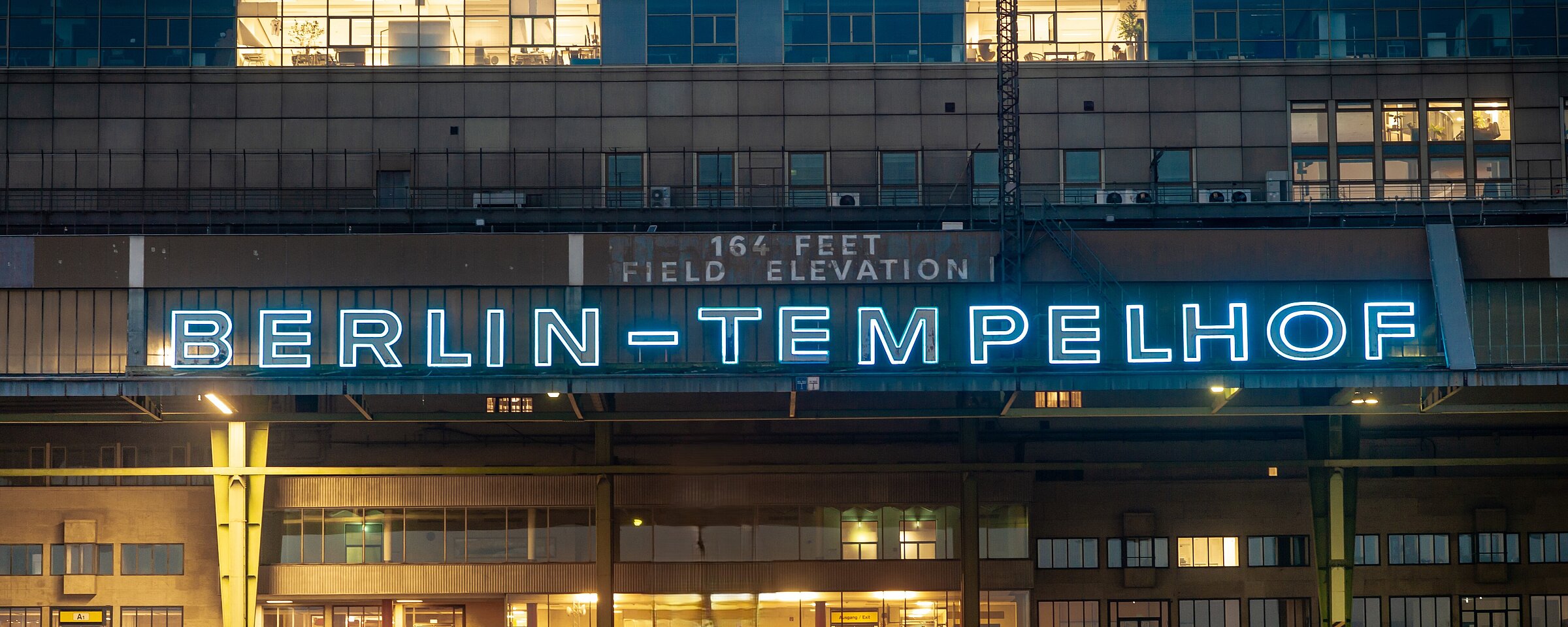 Fassade des Flughafen Tempelhof mit dem Ikonischen Schriftzug "Berlin-Tempelhof", der in der Dämmerung blau leuchtet