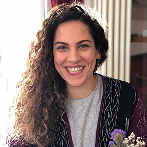 Porträt von Shadi Tabibzadeh, die vor einer Heizung sitzt und in die Kamera schaut