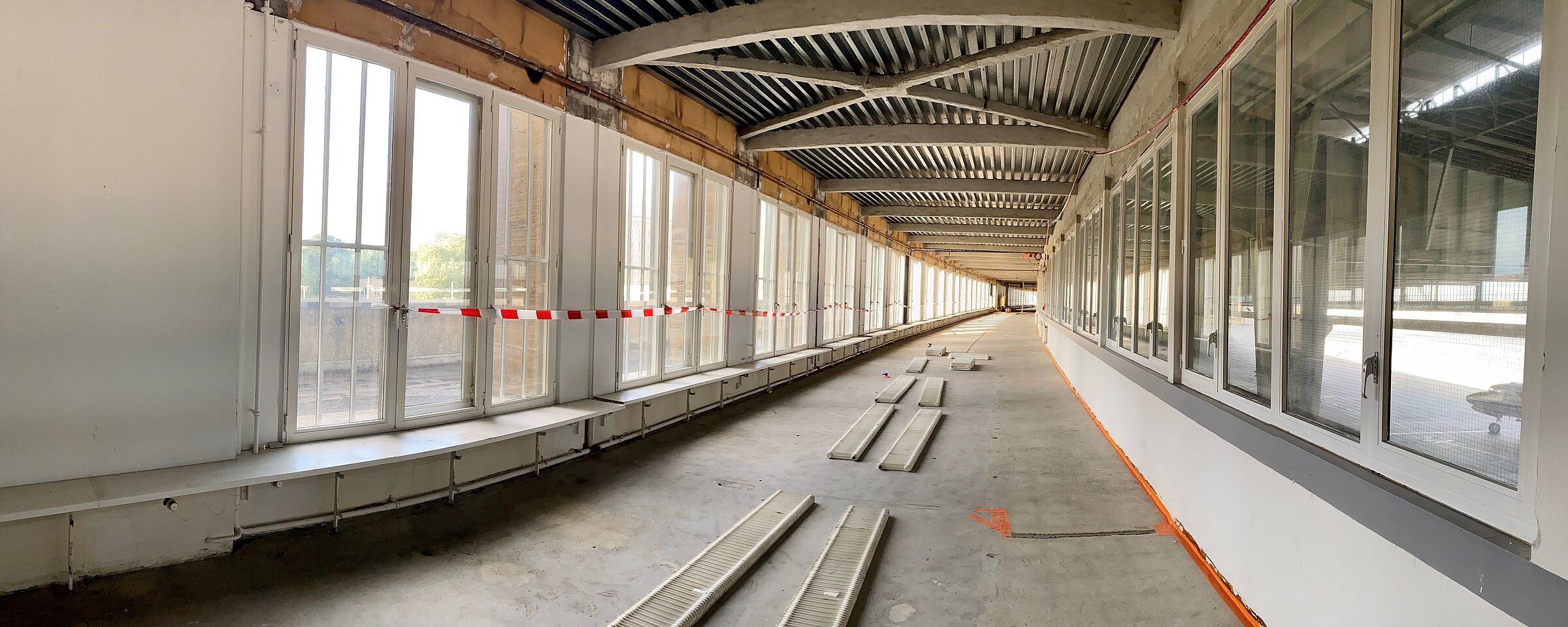 Blick auf den Rohbau eines langen Gangs am Flughafen Tempelhof, links und rechts sind große Fenster mit Blick auf das Vorfeld