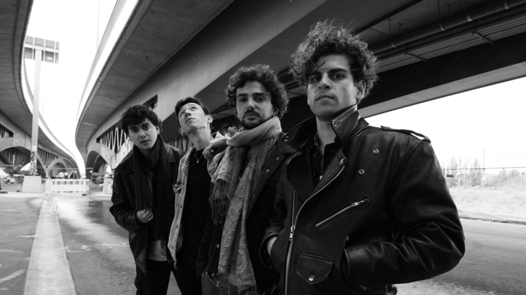 Schwarz-Weiß-Fotografie der vierköpfigen Band full red grenade, die in einer urbanen Umgebung posiert. Die Bandmitglieder stehen im Vordergrund unter einer massiven Betonkonstruktion einer Überführung oder Brücke.