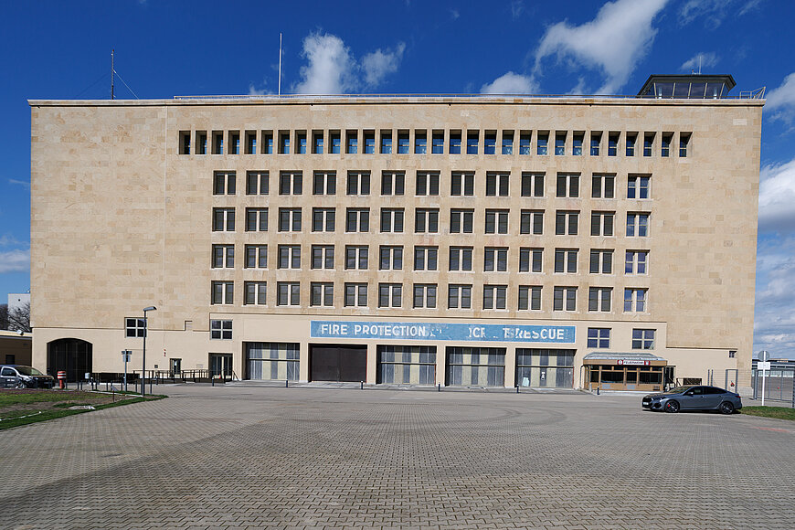 Außenfassade des THF TOWER mit blauem "Fire Protection"-Schriftzug. Vor dem Gebäude steht rechts ein Auto